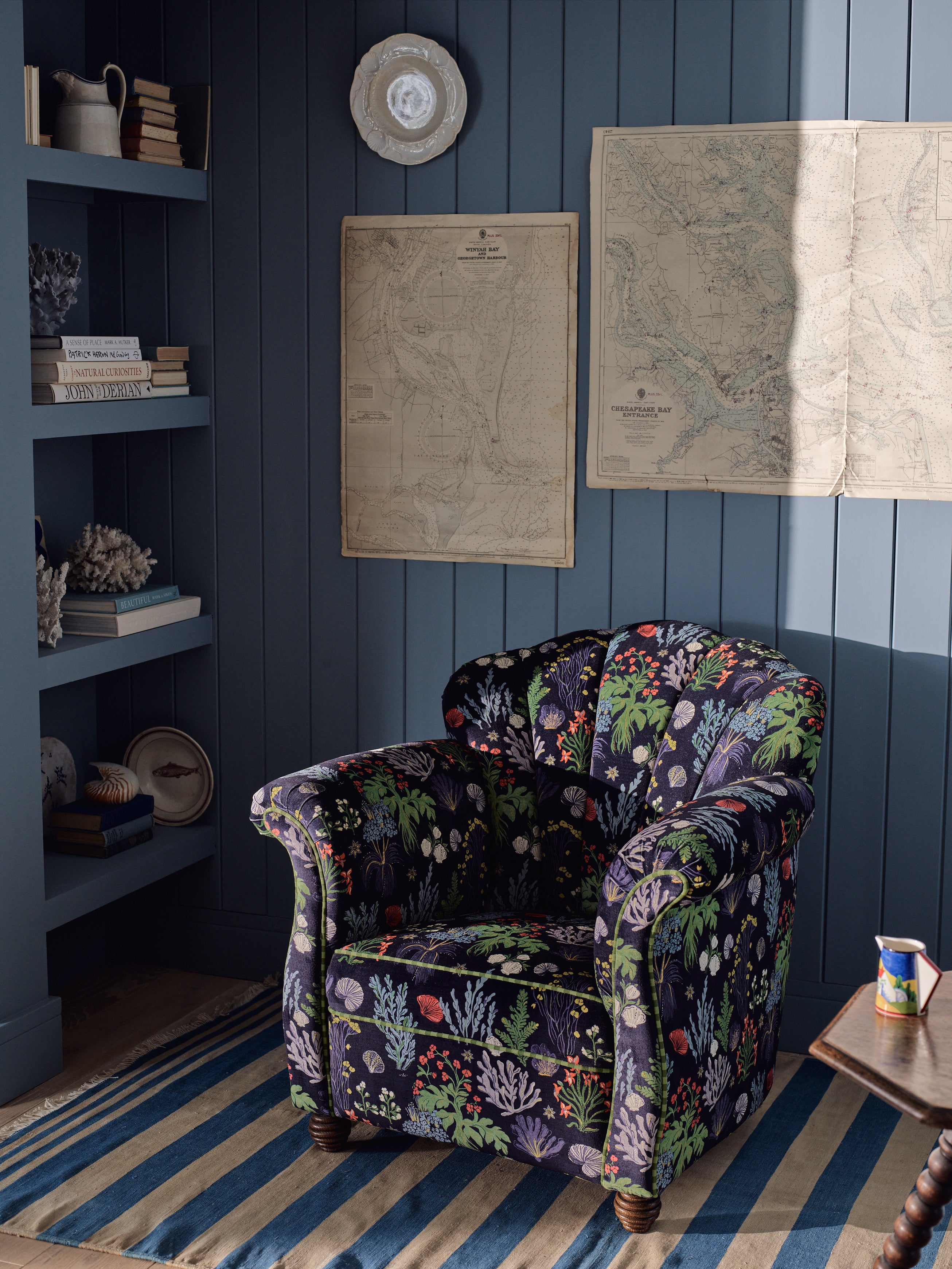 Floral-patterned armchair in a room with blue walls, striped rug, and vintage maps.
